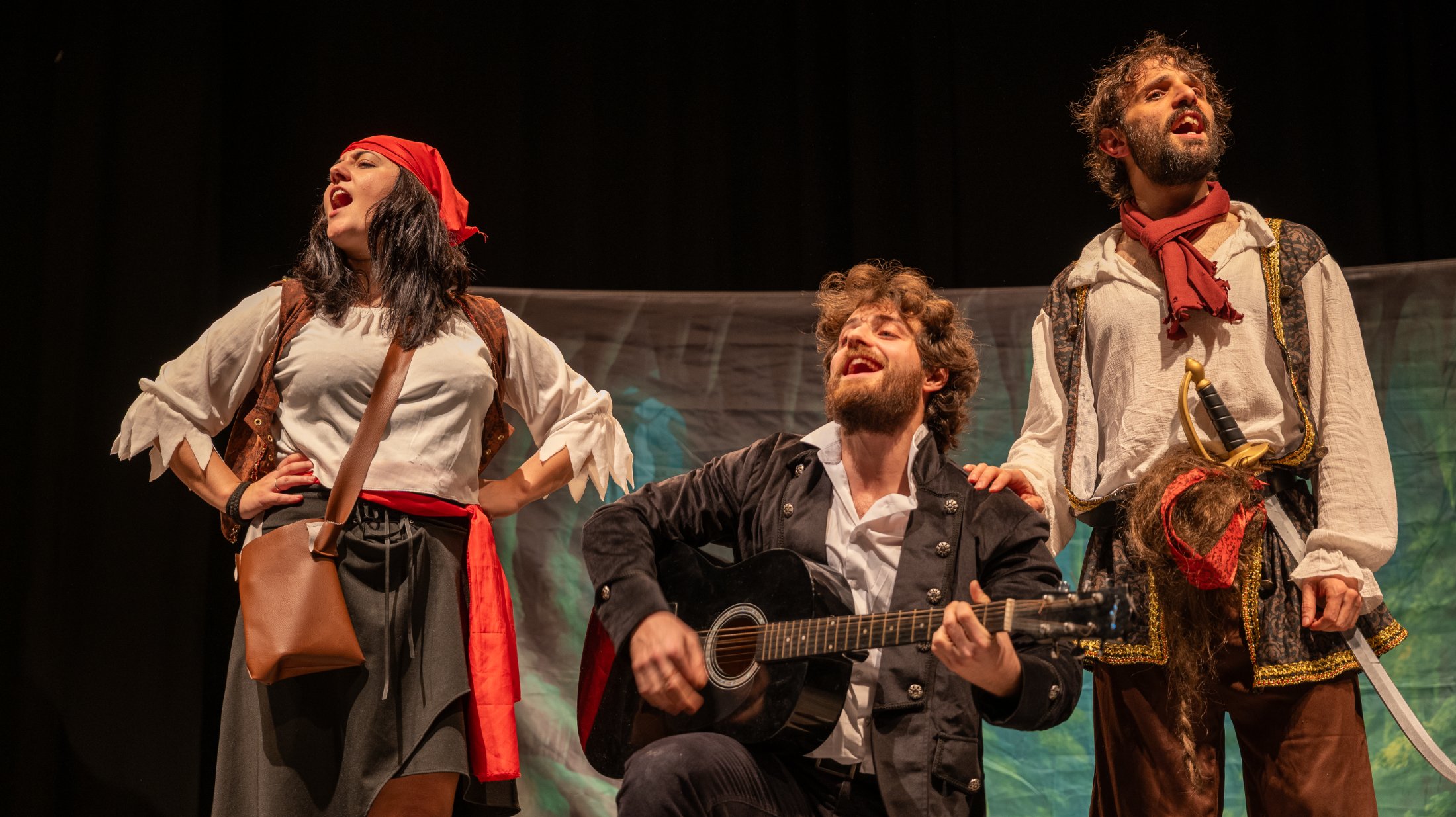 Tre attori in costume cantano sul palco